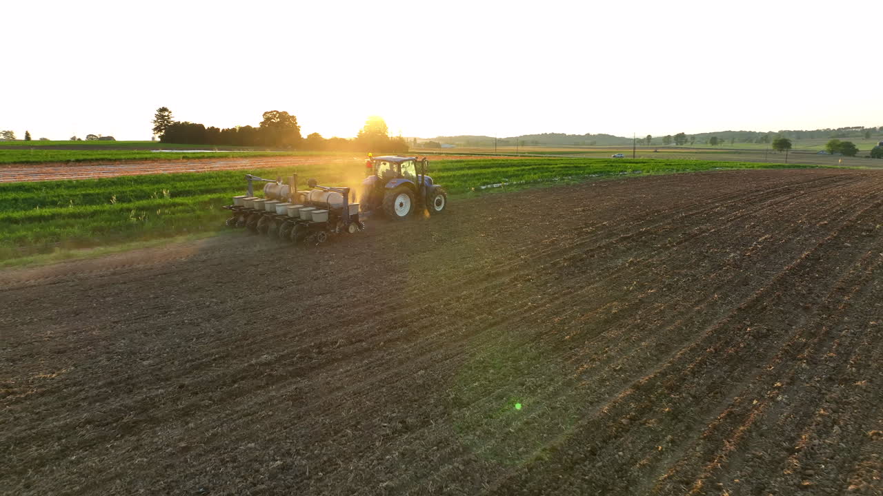 Aerial descent towards planter being pulled by New Holland tractor. Beautiful golden hour light during spring sunset. Dirt in air from seeder