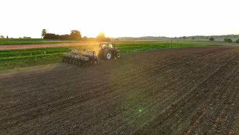 aerial descent towards planter being pulled by new holland tractor. beautiful golden hour light during spring sunset. dirt in air from seeder