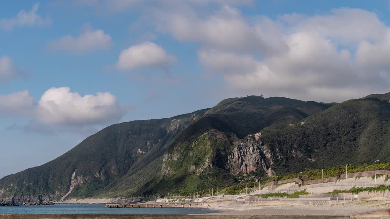 lapso de tiempo de nube en movimiento rápido proyectando sombra sobre acantilados verdes con el océano y la playa en primer plano - empujar hacia adentro