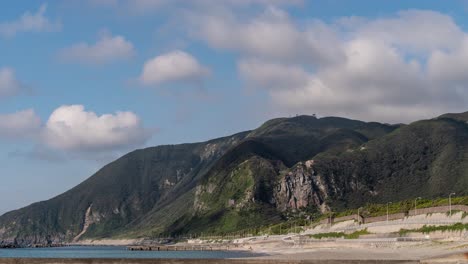 Fast-moving-cloud-timelapse-casting-shadow-on-green-cliffs-with-ocean-and-beach-in-foreground---Push-In