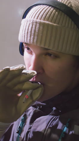 primer plano de un atleta con chaqueta de invierno con auriculares y guantes fumando al aire libre con una expresión enfocada e introspectiva