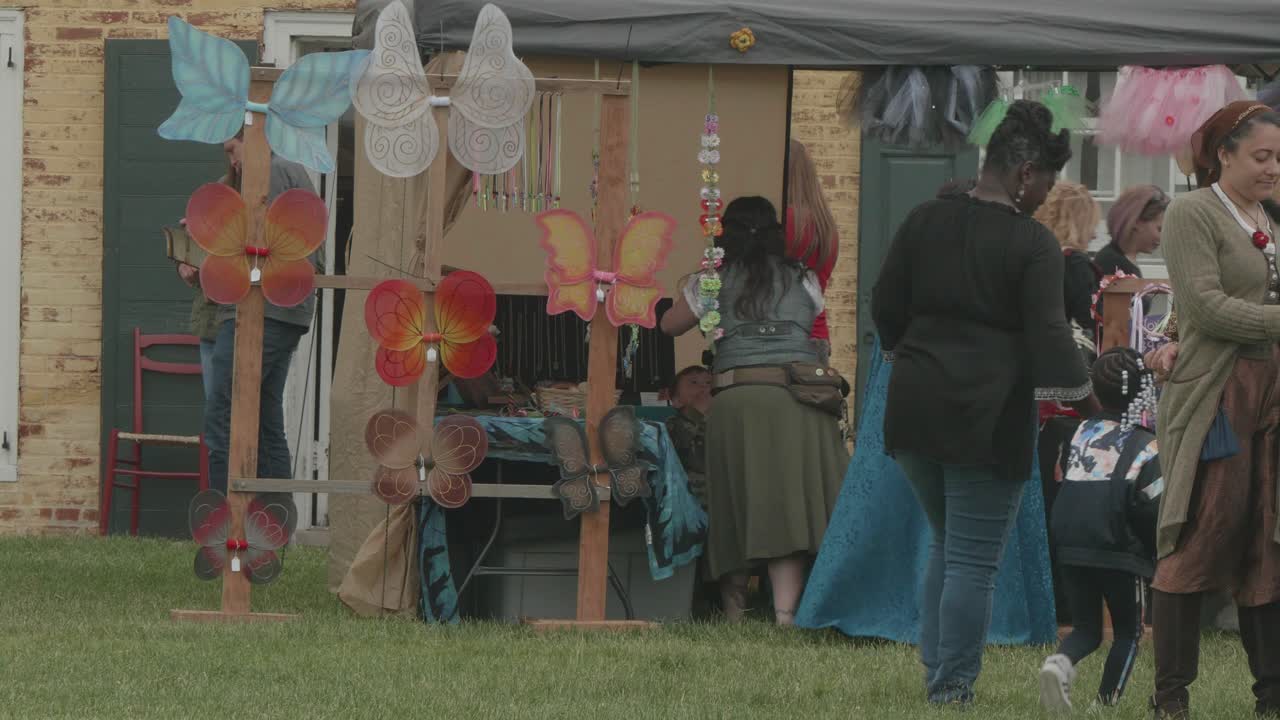 An outdoor market featuring craft stalls with butterfly wings and people browsing