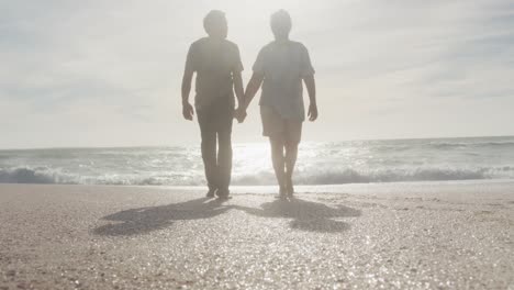 latin hispanic couple holding hands, walking on beach at sunset