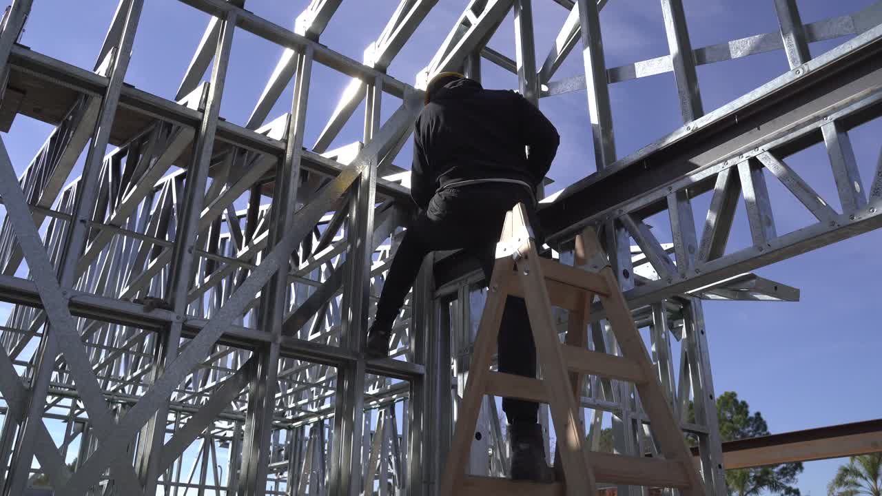 4K30 man standing on a ladder building a steel frame house