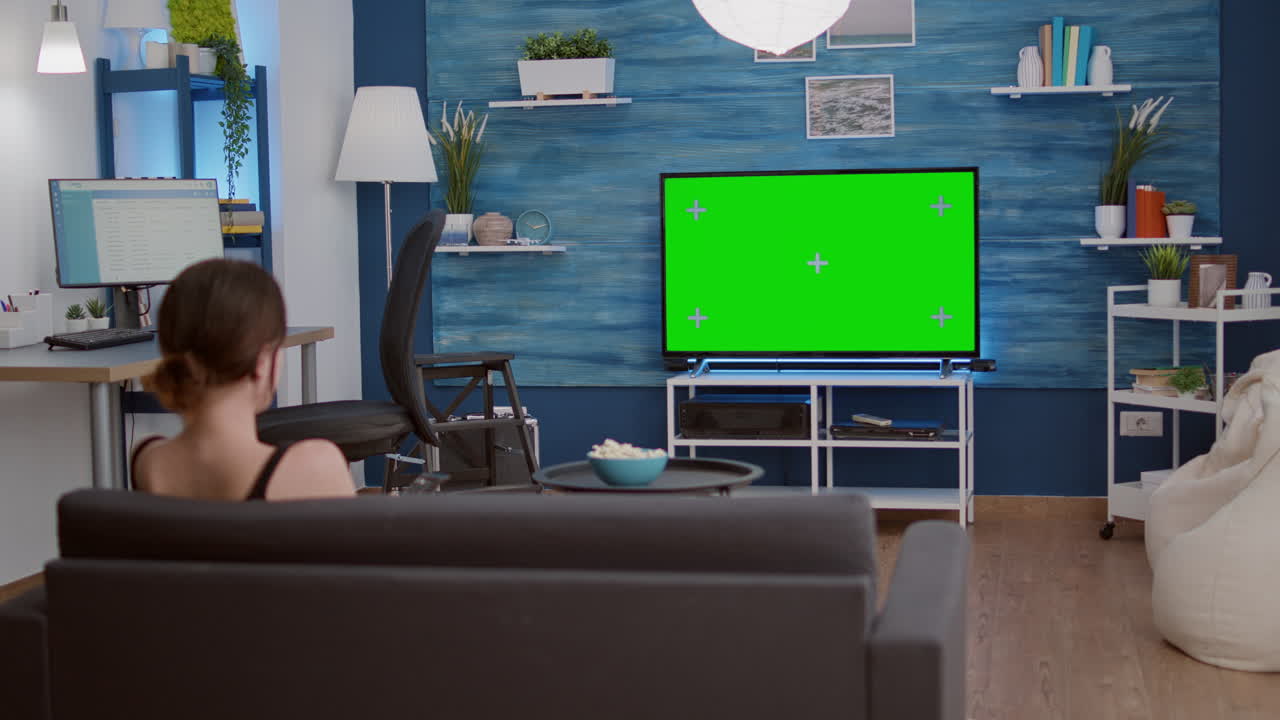 Static tripod shot of young woman zapping tv lookin for favourite show while looking at green screen