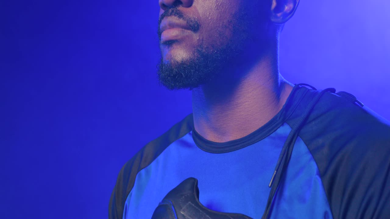 Telecamera che si alza rivelando il volto di un uomo africano in maglia blu, in piedi, che tiene una scarpa da calcio in studio.