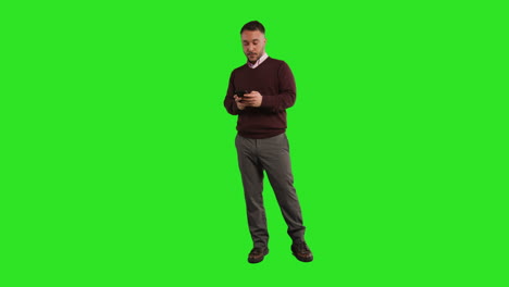 Full-Length-Studio-Portrait-Of-Mature-Male-Teacher-Or-Businessman-Standing-Against-Green-Screen-Using-Mobile-Phone-To-Message-Or-Browse-Online-1