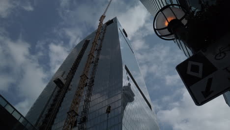 Low-angle-wide-shot-looking-up-at-a-tall-building-with-a-crane-lifting-a-load-skywards