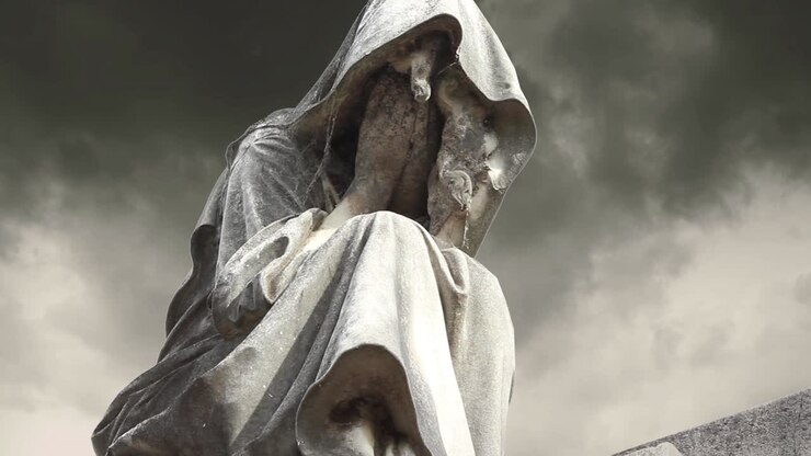 Malinconica statua di pietra di una figura incappucciata in lutto