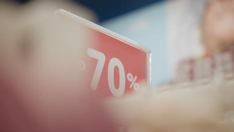 price sign showing seventy percent discount in retail clothing store with blurred racks of jackets in setting, red display board with white typography under ambient lighting for winter clearance sale