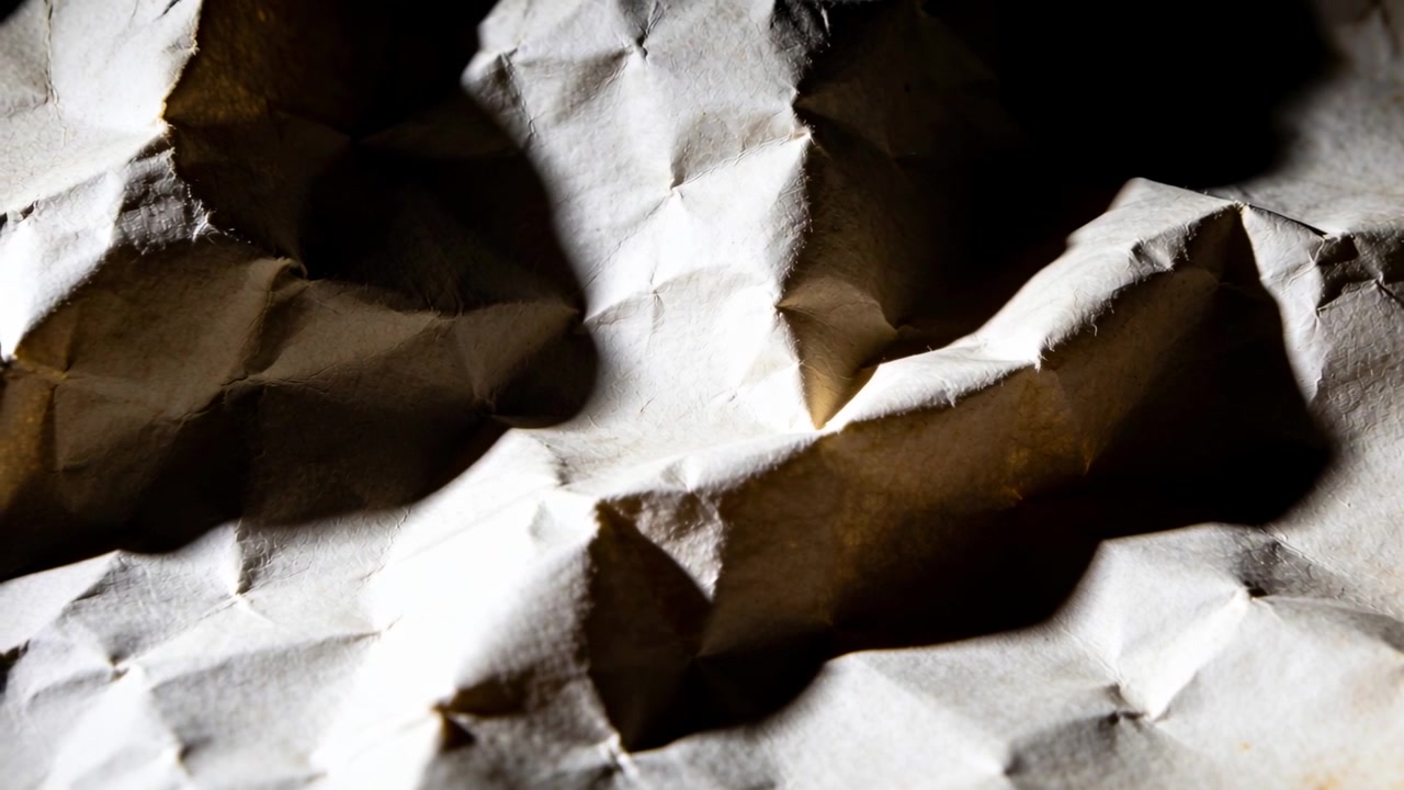 Shifting lamp casting shadows across crumpled white sheet on studio table, revealing deep creases