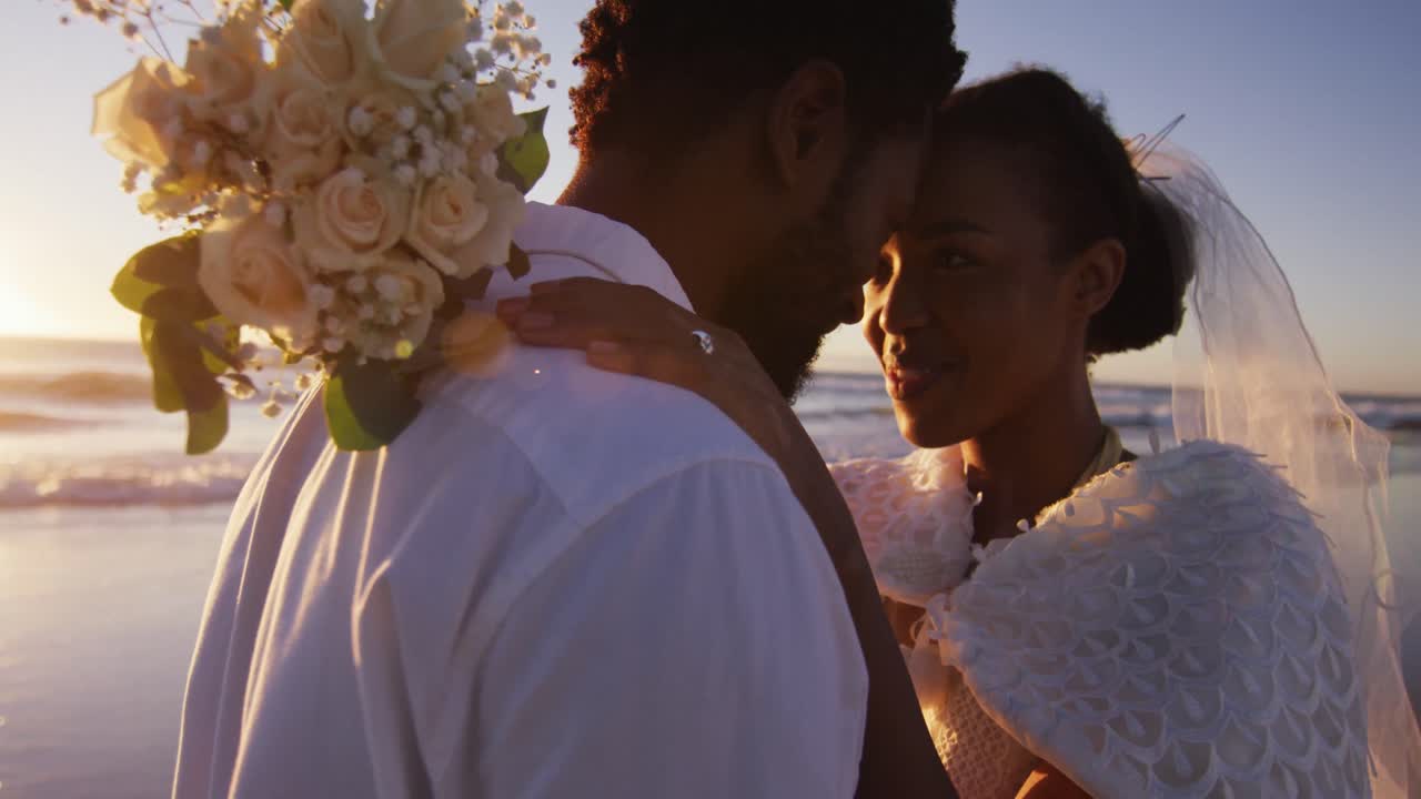African american couple in love getting married, looking at other on the beach at sunset