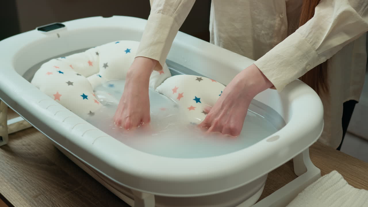 Persona preparando el baño de un bebé con un cojín suave en una bañera portátil, comprobando la temperatura del agua
