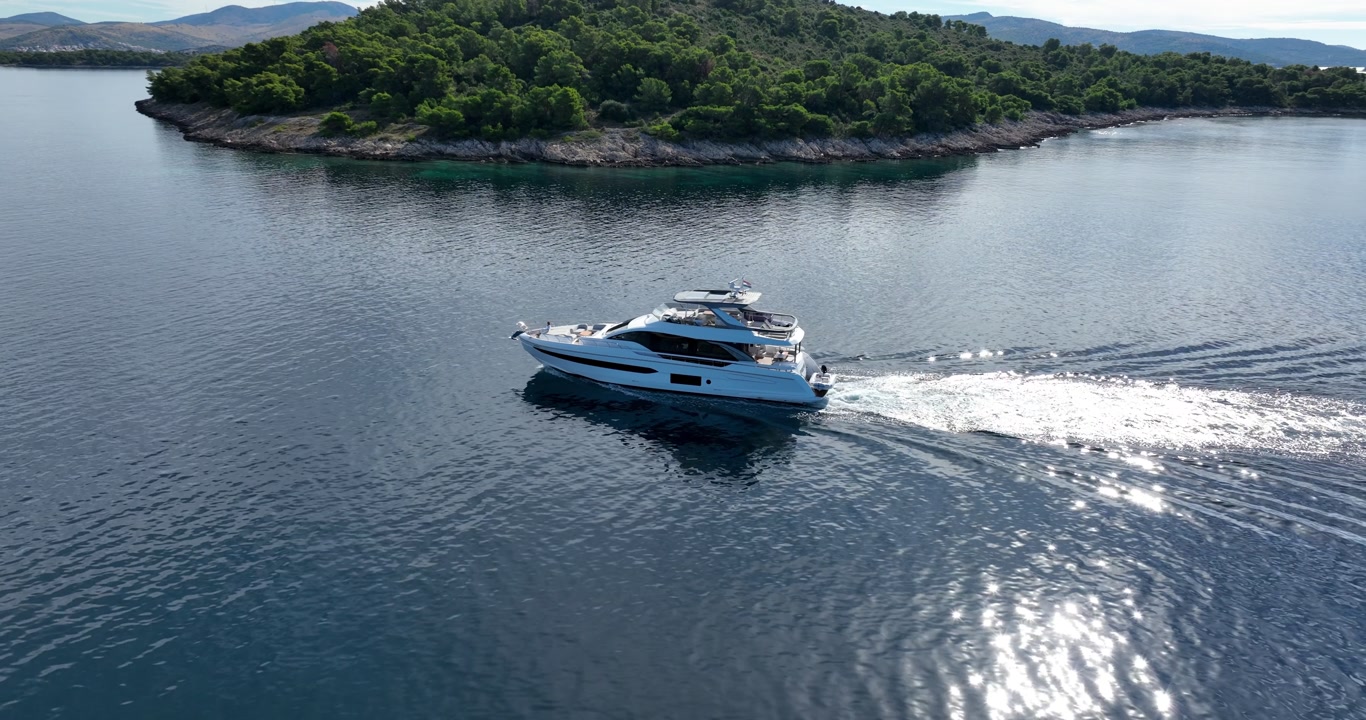 Stunning aerial footage of modern luxury yacht sailing through calm blue Adriatic waters near lush forested island coastline in Sibenik, Croatia.