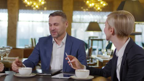 Dos-Empresarias-Y-Un-Hombre-De-Negocios-Hablando-En-El-Desayuno-Sentados-En-Una-Mesa