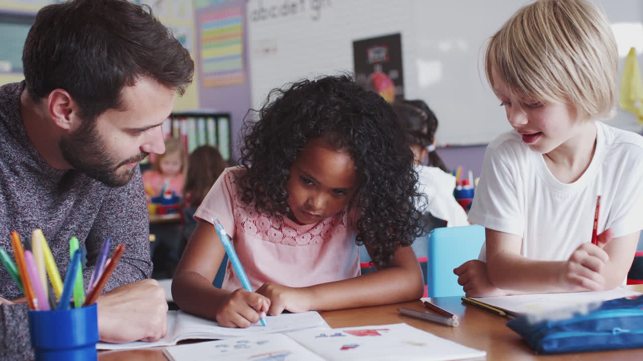 maestro de escuela primaria sentado en el escritorio ayudando a los alumnos en el aula