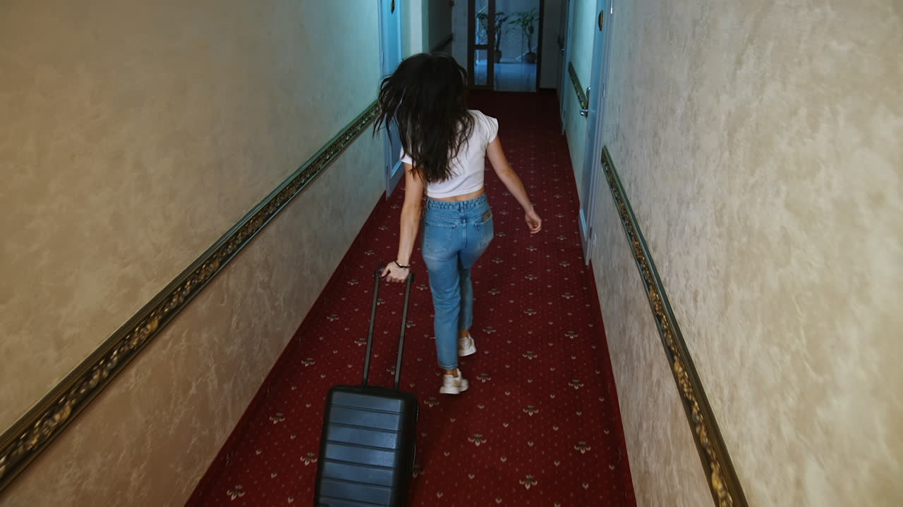 Woman holding a suitcase in hotel corridor. Cute happy girl moved in a hotel and is looking for her room.