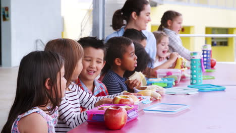 niños de la escuela primaria y el maestro en una mesa en la pausa del almuerzo