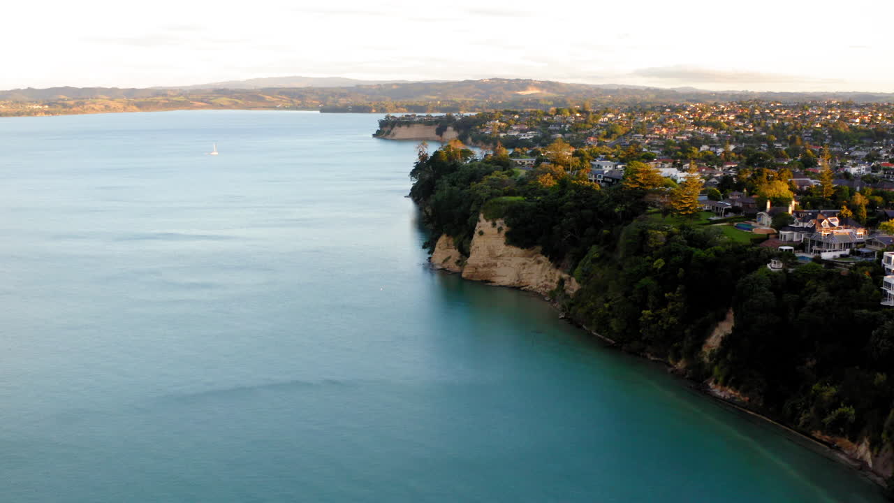 Aerial view of a coastal town with houses atop cliffs overlooking the ocean and a sailboat