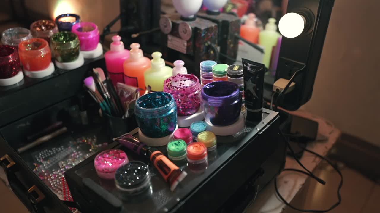 Estación de maquillaje de fiesta con purpurina en un evento de cumpleaños donde se muestran pigmentos coloridos, polvos brillantes, pinceles y frascos de cosméticos dispuestos para un arte facial creativo, estilismo de belleza festivo, dolly in shot