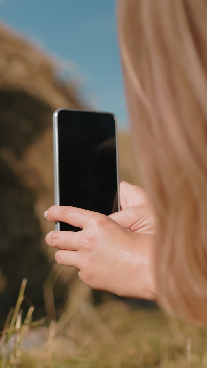 mujer tomando una foto con un teléfono inteligente de un amigo acostado en el heno con las piernas levantadas en el aire, un entorno al aire libre soleado en un campo rural, capturando un momento divertido y relajado en la naturaleza