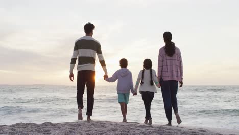 Back-view-of-hispanic-family-standing-on-beach-at-sunset