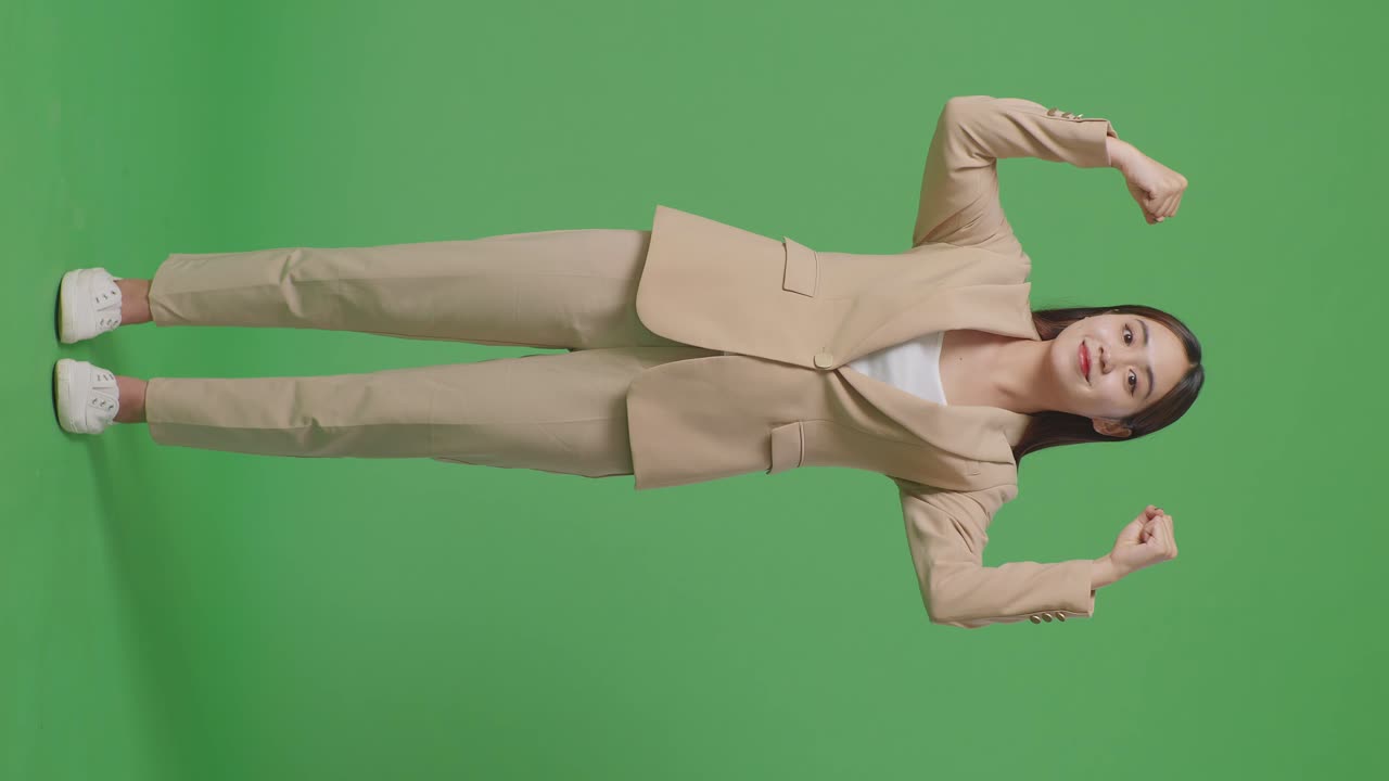 아시아 사업가 여성의 몸이 가득 차 있으며 스튜디오의 녹색 스크린 배경에서 미소 짓고 근육을 구부립니다.