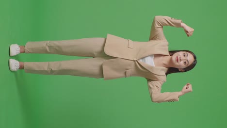 아시아 사업가 여성의 몸이 가득 차 있으며 스튜디오의 녹색 스크린 배경에서 미소 짓고 근육을 구부립니다.
