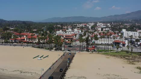 Drone-Aéreo-De-Autos-Cruzando-El-Muelle-Stearns-Wharf-En-El-Centro-De-Santa-Barbara-En-Un-Soleado-Día-De-Verano-En-California-Con-Grandes-Montañas-En-La-Distancia