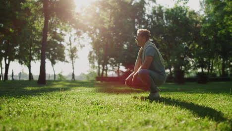 attractive stylish man sitting in squat in park. relaxed guy look in distance