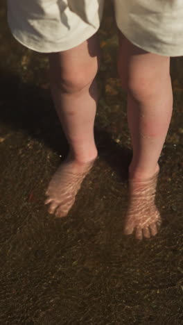 children stand barefoot in water on dark sand in tourist area. comfortable water temperature for relaxation on sunny day. spending leisure time together