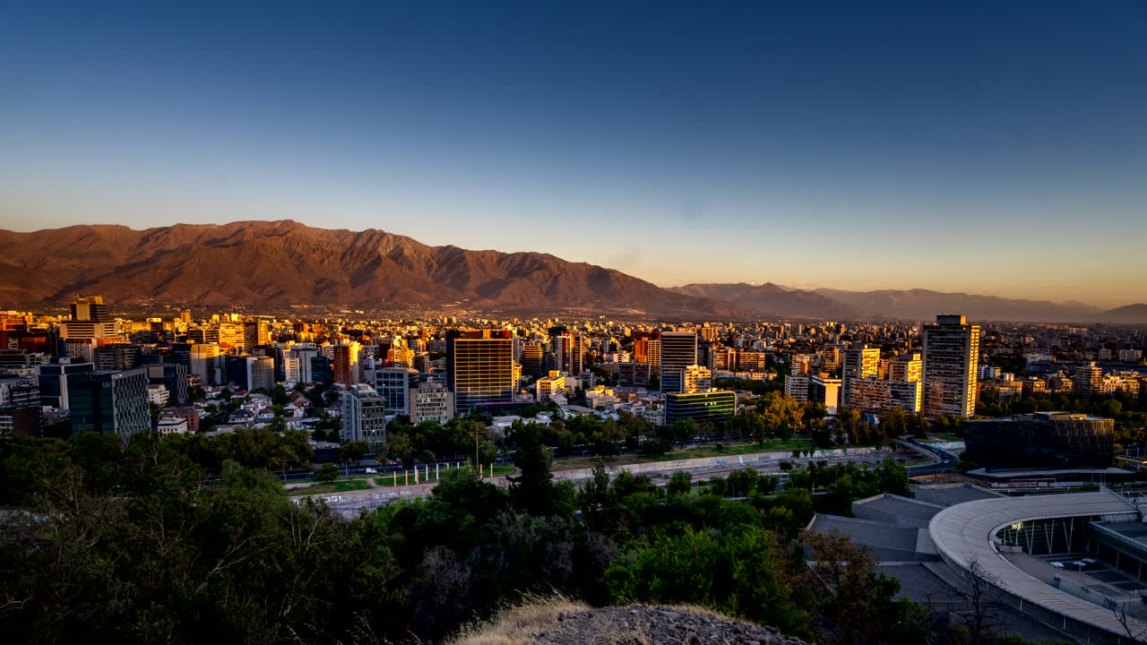 Santiago skyline as sunset light recedes to dusk night glow with buildings lighting up and clouds moving fast in time lapse, day to dusk