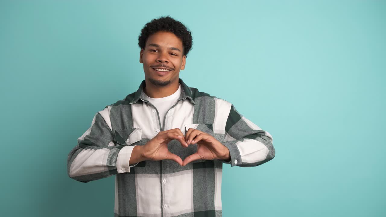 Giovane uomo felice che fa il gesto del cuore su sfondo blu