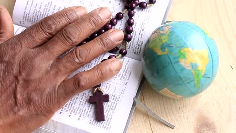 Beten-Zu-Gott-Mit-Der-Hand-Auf-Der-Bibel-Mit-Kreuz--Und-Erdballhintergrund-Mit-Leuten-Stock-Footage