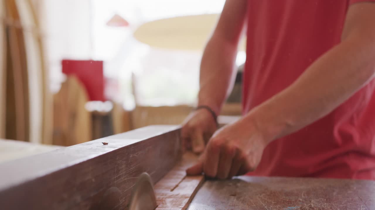 fabricante de tablas de surf masculino caucásico trabajando en su estudio y haciendo una tabla de surf de madera