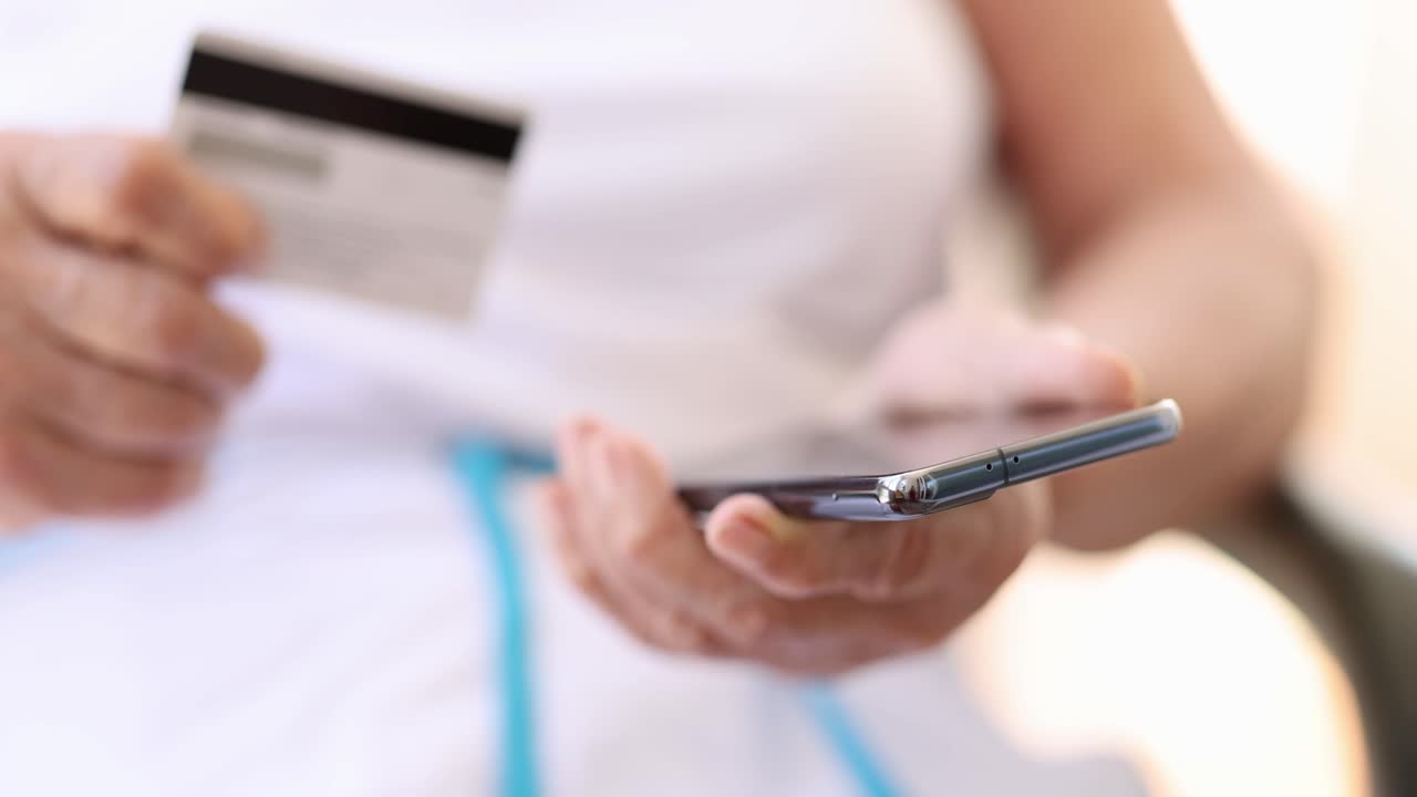 Donna anziana tiene in mano la tessera della pensione e lo smartphone.