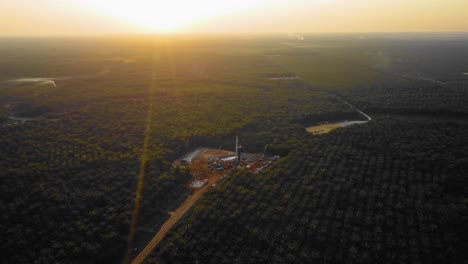 Cinematic-4K-Drone-Footage-of-Onshore-Drilling-Rig-equipment-structure-for-oil-exploration-and-exploitation-in-the-middle-of-jungle-surrounded-by-palm-oil-trees-during-sunset-and-high-oil-price