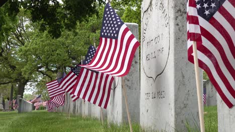 Nahaufnahme-Der-Grabsteine-Auf-Einem-Friedhof-Mit-Überresten-Von-Bürgerkriegssoldaten-Am-Gedenktag,-Während-Amerikanische-Flaggen-Im-Wind-Flattern