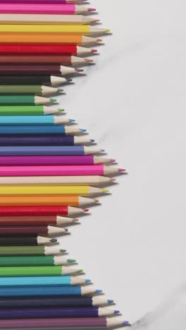 Vertical-Video-Of-Coloured-Pencils-Arranged-In-A-Symmetrical-Pattern-On-White-Marble-Background-