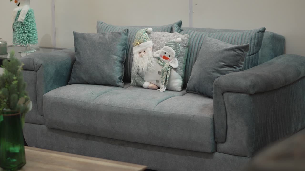Close-up of grey couch decorated with Christmas pillow and seasonal ornaments in living room.