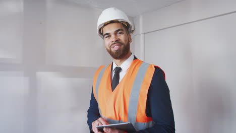 portrait of surveyor in hard hat and high visibility jacket with digital tablet carrying out house inspection