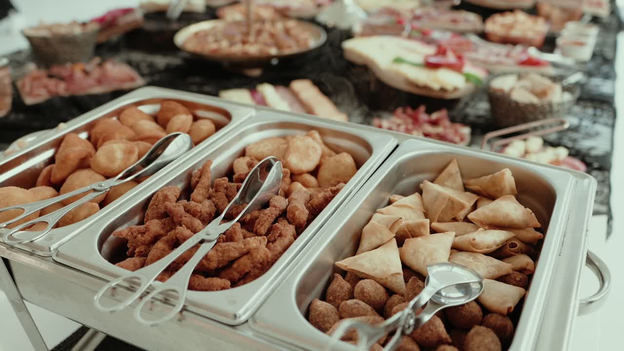 crispy assorted snacks like samosas and fritters in metal buffet trays at a catered event