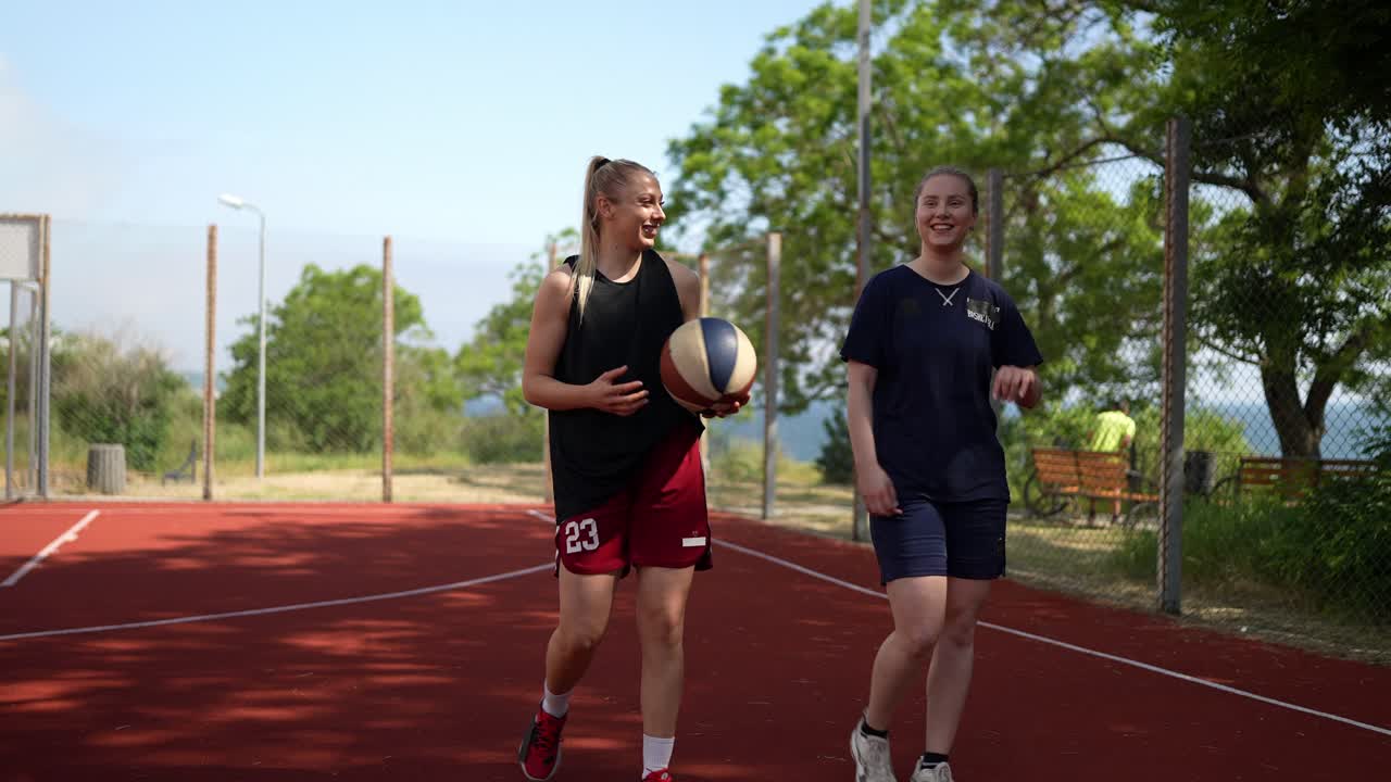 두 명의 여성이 야외 코트에서 농구를 하고 있다.