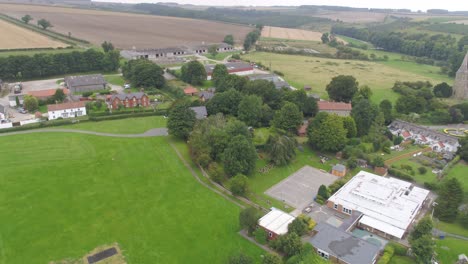 Imágenes-En-Movimiento-De-Drones-De-Un-Pueblo-Muy-Pequeño-En-La-Zona-Rural-De-Yorkshire,-Inglaterra,-Reino-Unido,-Que-Incluye-Una-Escuela,-Una-Granja,-Una-Iglesia-Y-Casas,-Todo-Ello-Rodeado-De-Campos-Y-Campos.