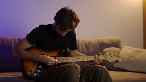 a man with a passion plays the guitar while sitting on the couch