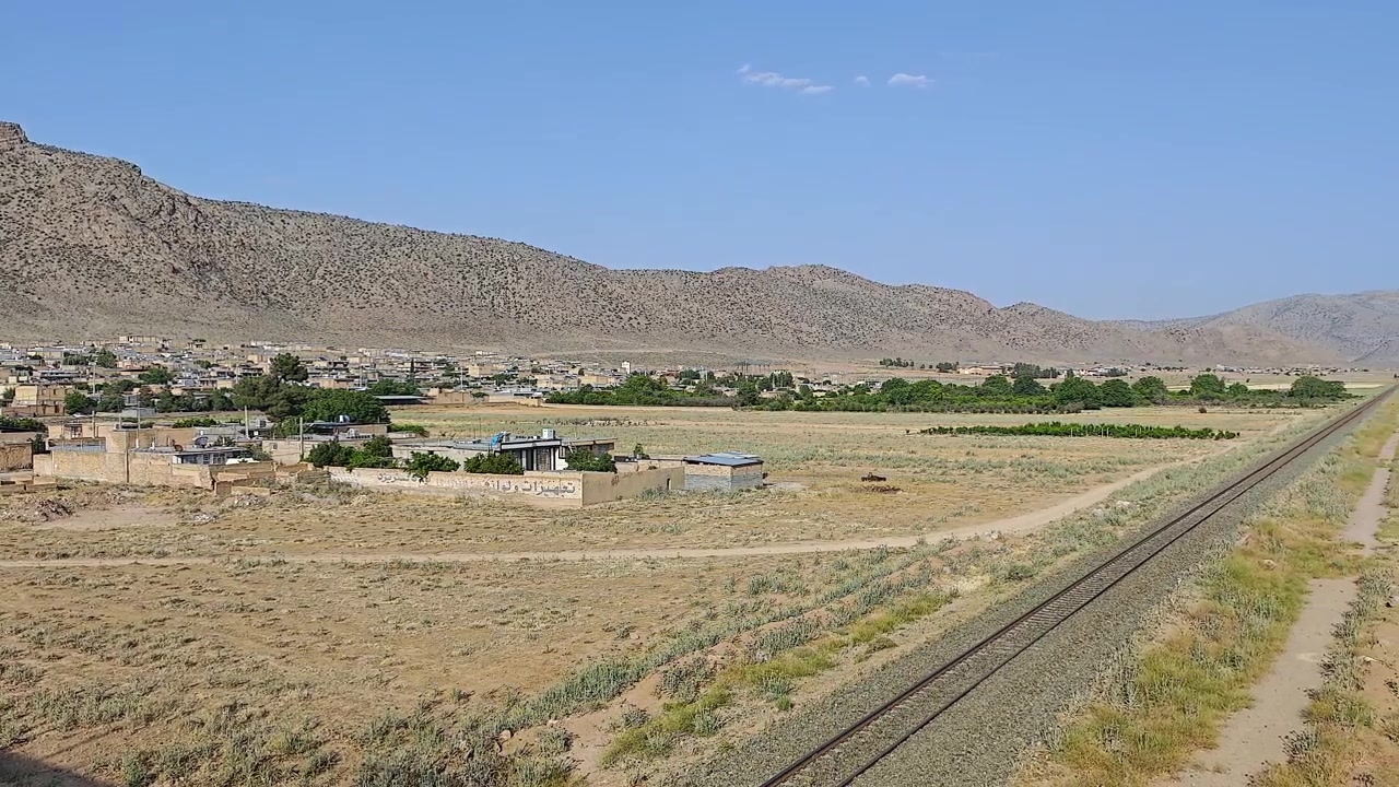 Vista panoramica di un villaggio rurale e binari ferroviari in un paesaggio desertico.
