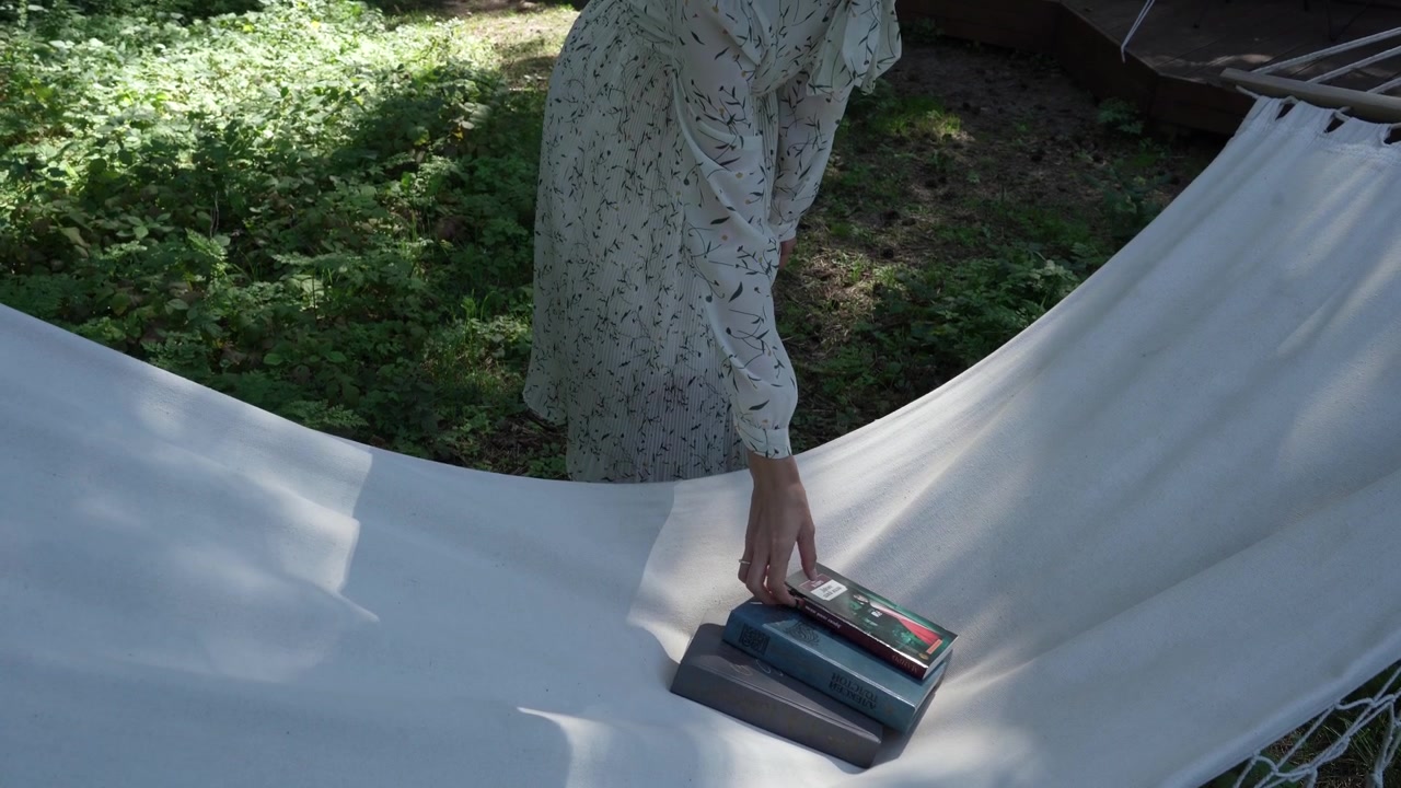 Ragazza in abito campagnolo bianco prende un libro da un'amaca in un glamping