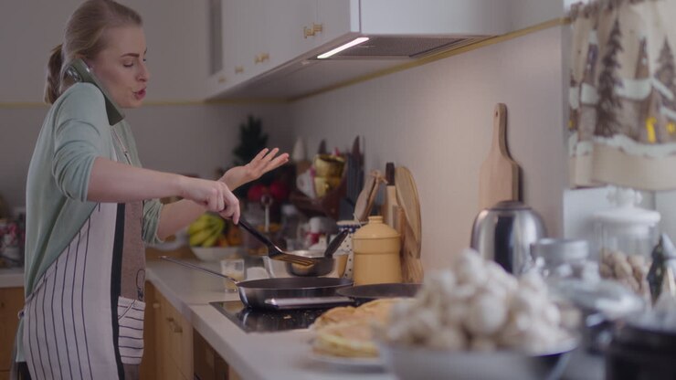 Donna turbata che lavora in cucina, parla al telefono e si innervosisce mentre cucina