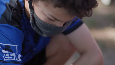 sad young boy wearing a covid-19 mask outside during the day in the shade