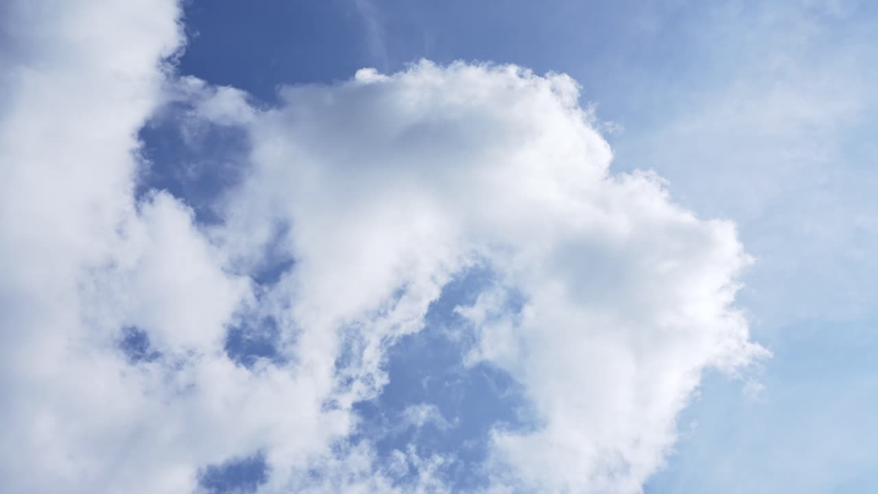 Timelapse of fluffy clouds drifting across a sunny blue sky